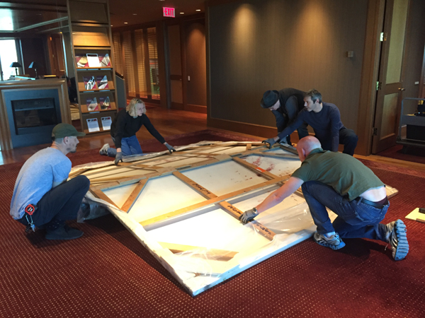 Dereck leading a team of technicians who are unfolding a large painting