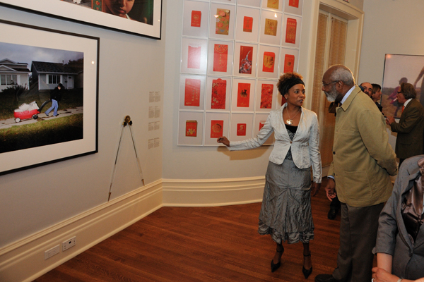 A woman is talking to a man and pointing to an artwork on the wall hung among other artworks.