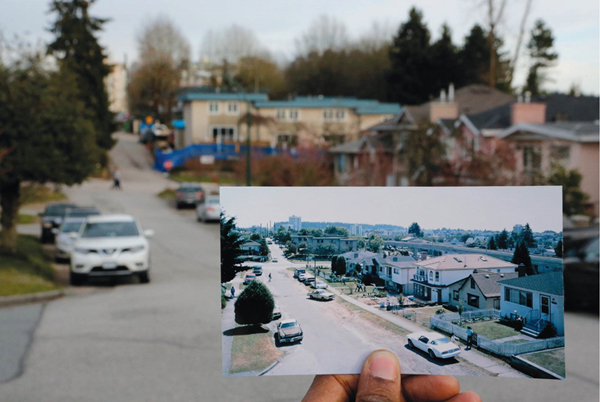 A photograph of a suburban neighborhood held up in front of the actual neighborhood.