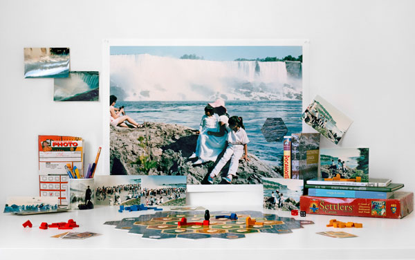 An enlarged photograph of people sitting on rocks in front of a waterfall paired with artifacts from the artist's childhood, research materials, family photos, and board games.