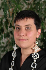 A headshot of woman with short dark hair wearing earrings that hang down past her shoulders.