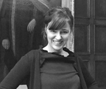 A headshot of a woman with dark hair pulled back into a ponytail wearing a black sweater over a black shirt.